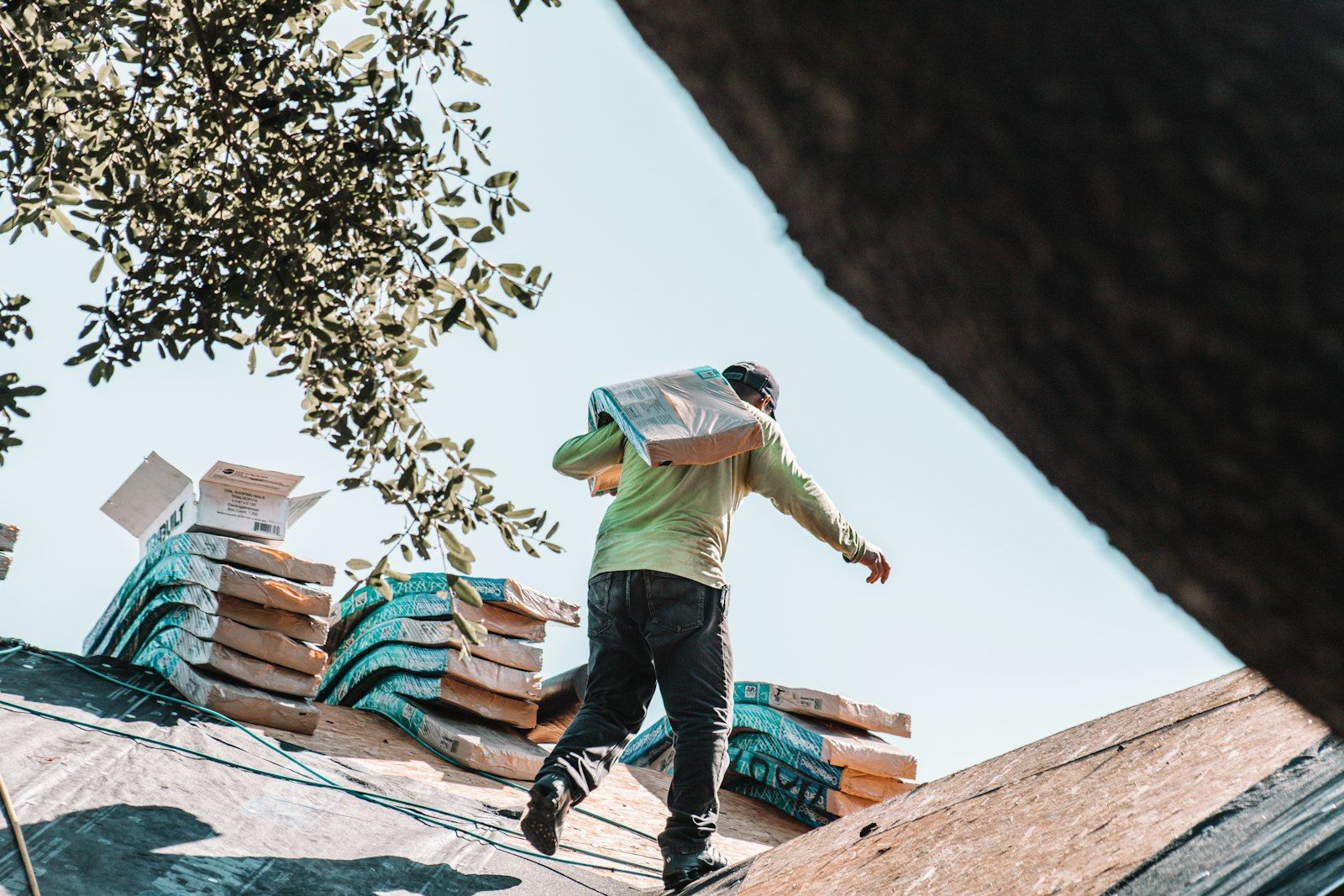 Roofer carrying a bundle of shingles across a residential roof.