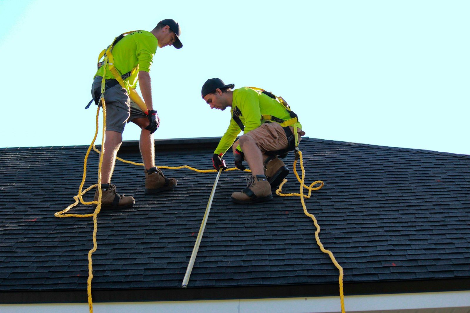 Two workers on a shingle roof.